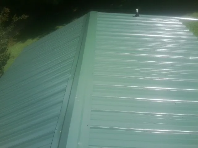 New green metal panels meeting at the ridge of a roof — Flat Roof Repair work by our crew in Monticello