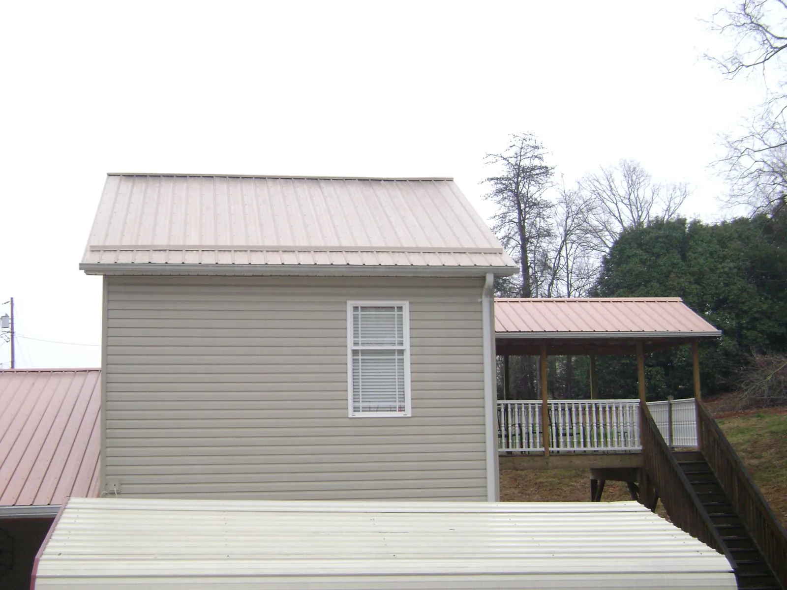 Tan metal roofs on a two story addition and attached porch, from a Roof Replacement job in Monticello